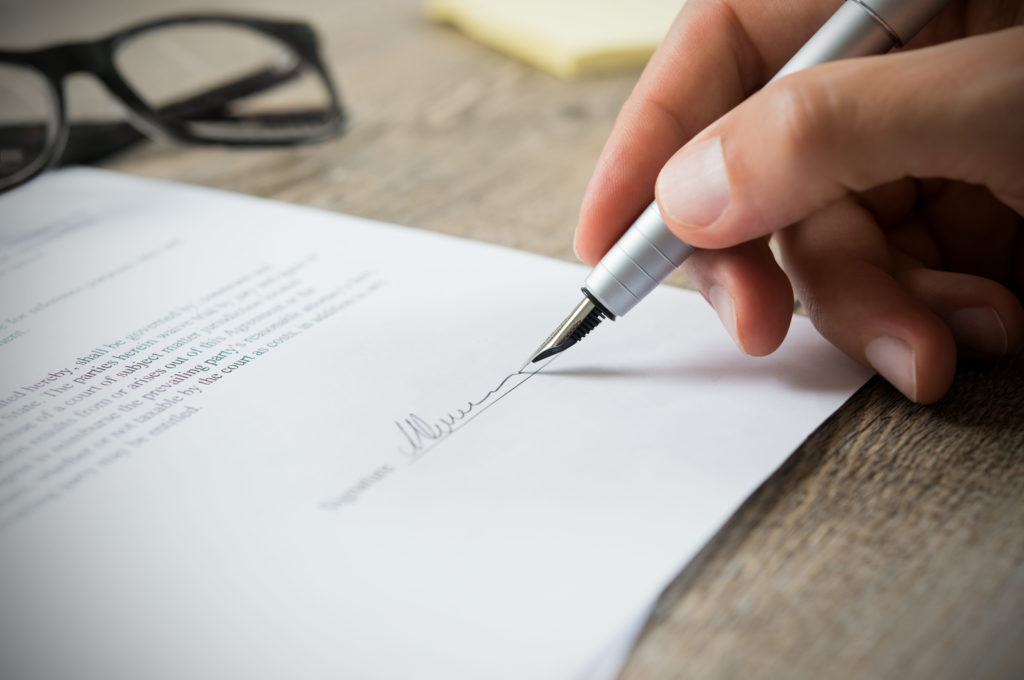 Close up of hand of businessman signing a form. Business man signing contract for future deal. Business man signing legal document. Male hand signing employee contract with a bond.